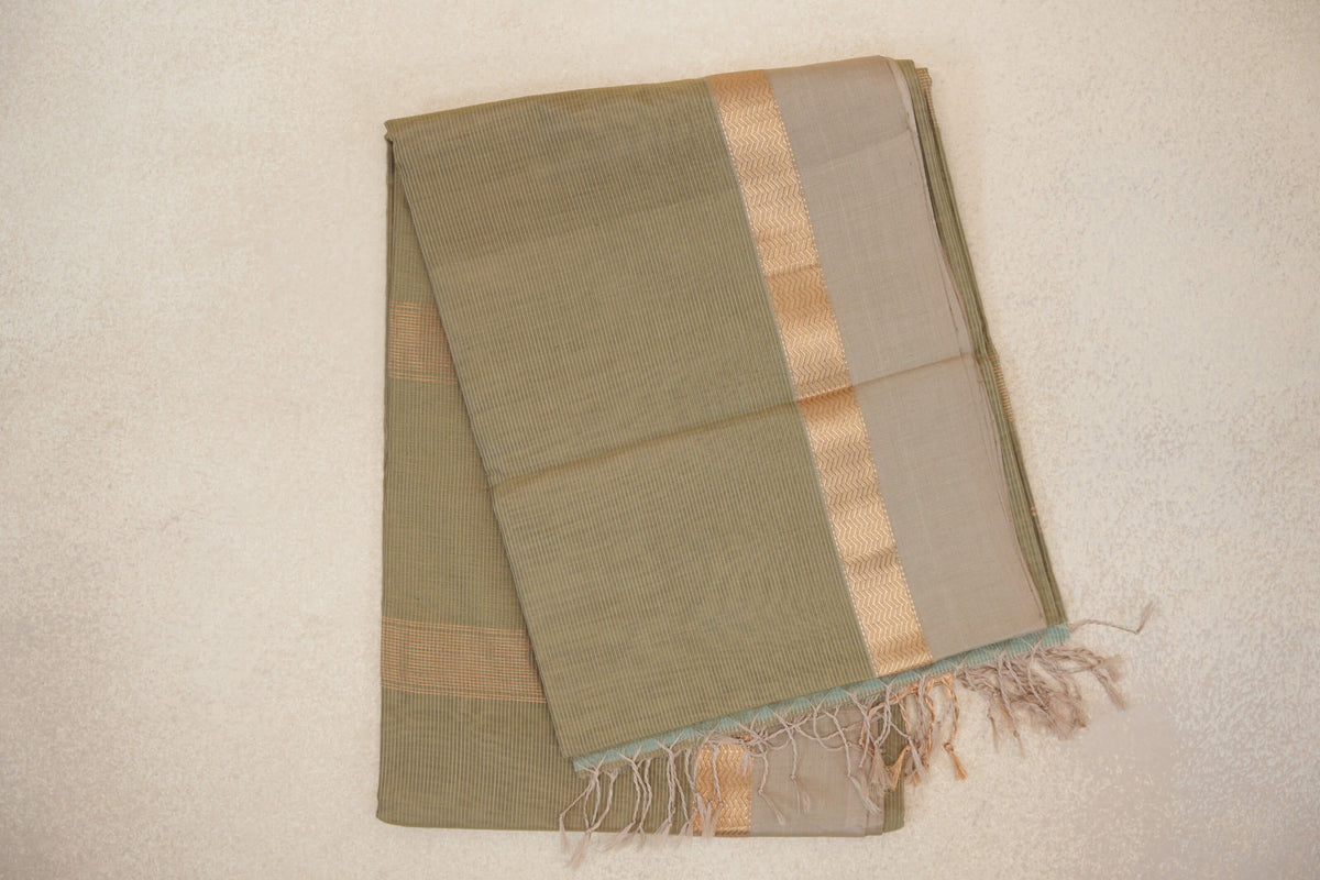 Folded light olive green Maheshwari silk cotton saree with fine stripes, a light beige border, a gold-toned zigzag band and tassels.