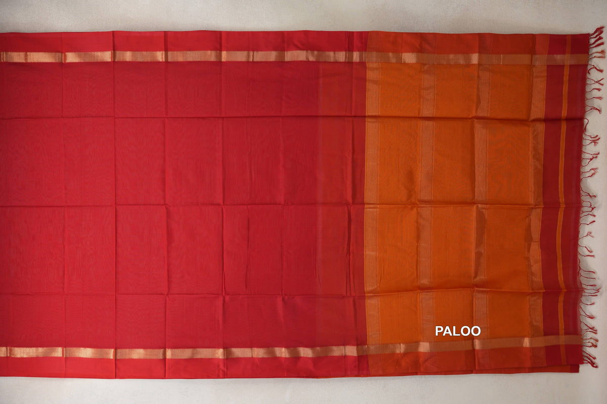 Maheshwari silk cotton saree laid flat, with a vermilion red body, narrow gold-toned borders and a deep orange pallu with fine stripes and tassels.