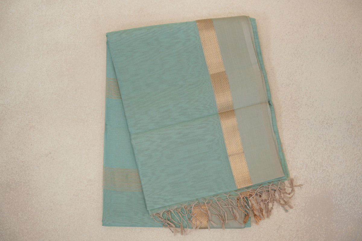 Folded sea green Maheshwari silk cotton saree with a fine checked weave, light sandal beige border, zigzag band and fringed end.