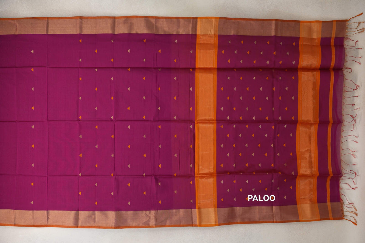 Deep magenta Maheshwari silk cotton saree laid flat, showing small triangular motifs, orange bands on the pallu, broad borders and tassels.