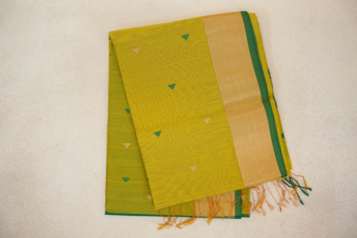 Folded bright lemon yellow Maheshwari silk cotton saree with small green and gold triangles, a broad gold-toned border, leaf green edge and tassels.