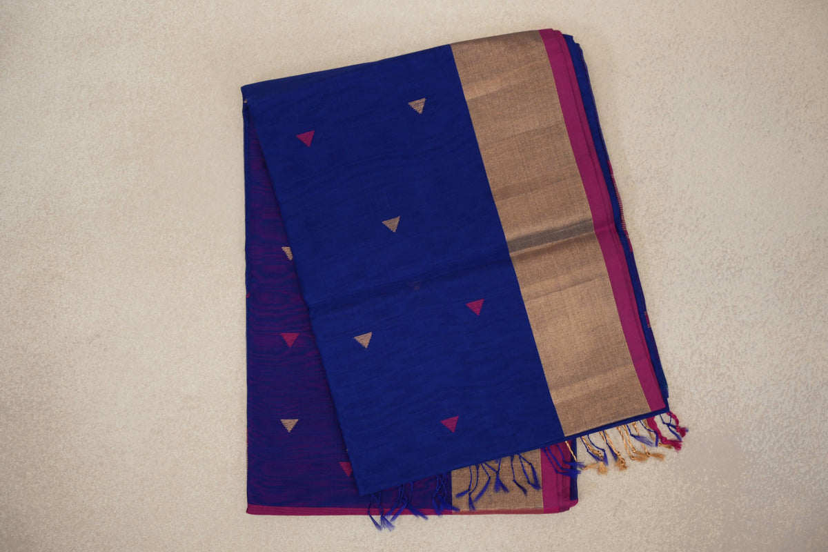 Folded bright royal blue Maheshwari silk cotton saree with small pink and gold triangles, a broad gold-toned border, rani pink edge and tassels.