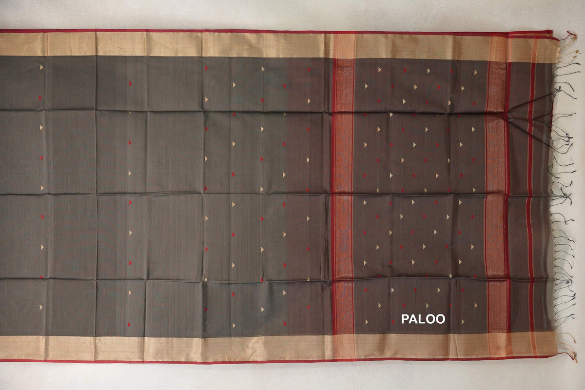 Maheshwari silk cotton saree laid flat, with a charcoal grey body, small red and cream triangles, beige borders with deep red edges, and a tasselled pallu.