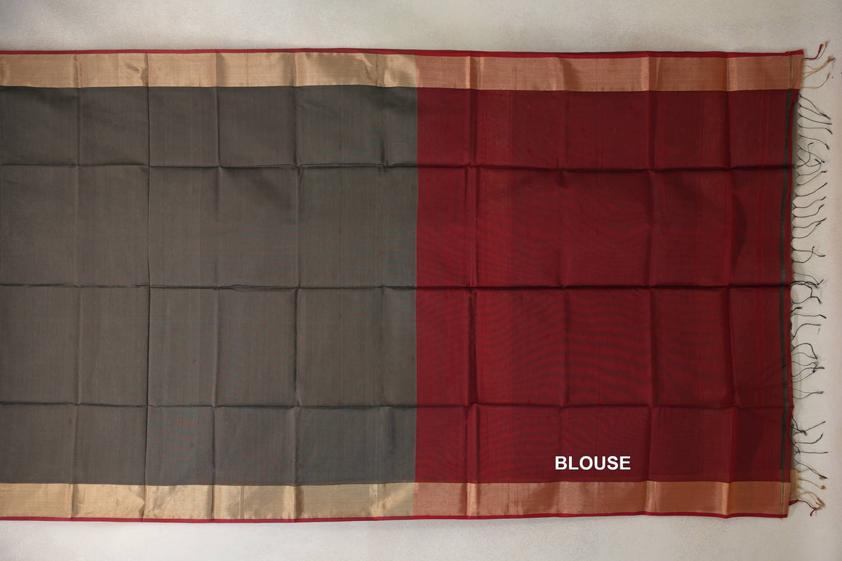 Laid-flat Maheshwari silk cotton saree showing a charcoal grey body beside a deep red blouse piece, with wide beige borders and end tassels.