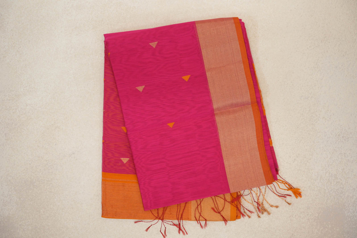 Folded Rani Pink Maheshwari silk cotton saree with small triangular motifs, a broad orange border and loose tassels.