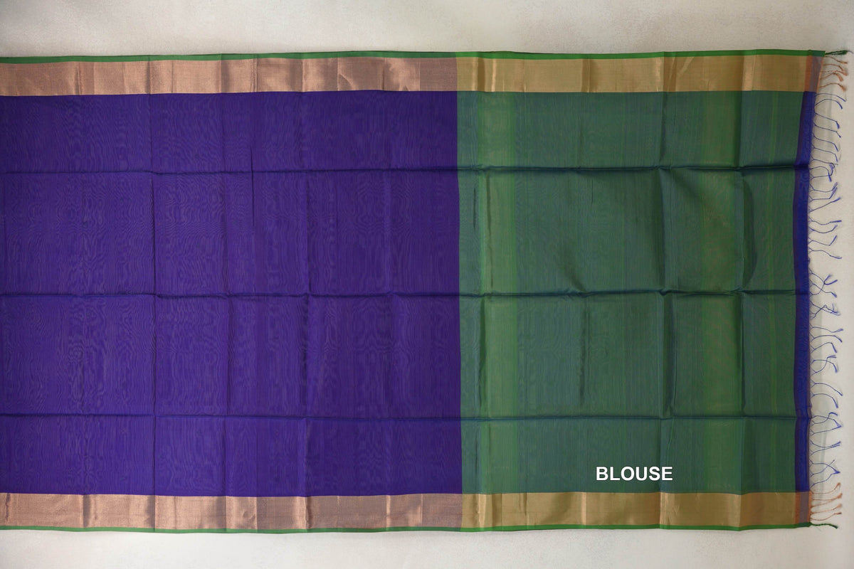 Maheshwari silk cotton saree laid flat, with a deep violet body, pale gold-toned borders with green edges, and a leaf green blouse section on the right.