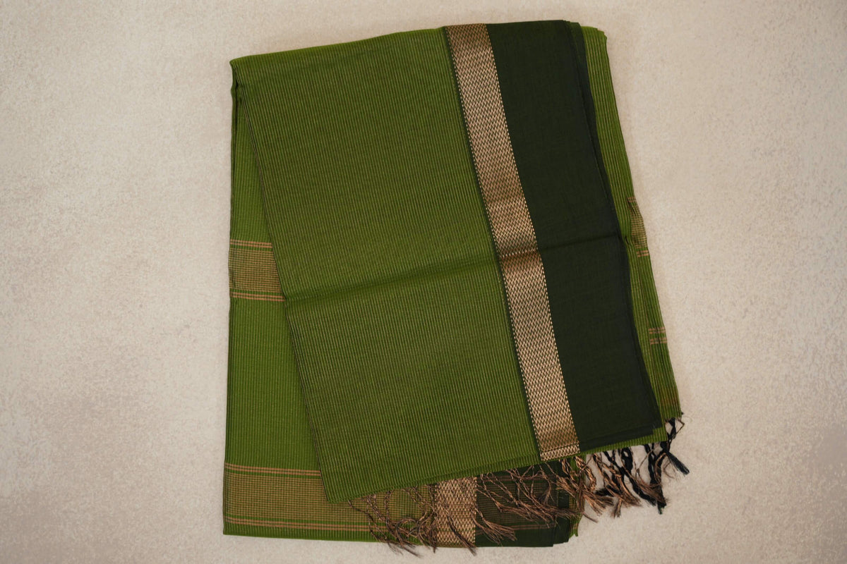 Folded olive green Maheshwari silk cotton saree with fine stripes, a deep forest green border, zigzag-patterned trim and tassels.