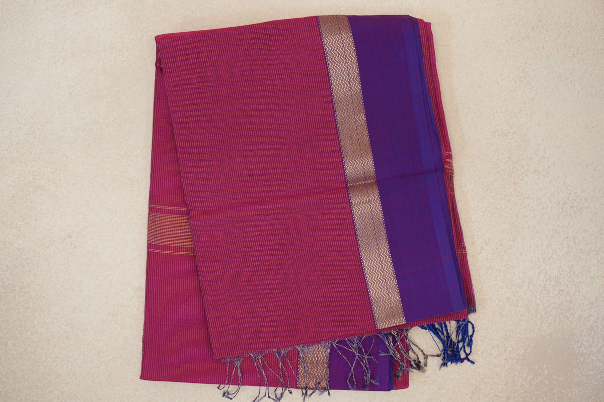 Folded deep rani pink Maheshwari silk cotton saree with fine stripes, a violet purple border, gold zigzag detailing and tassels.