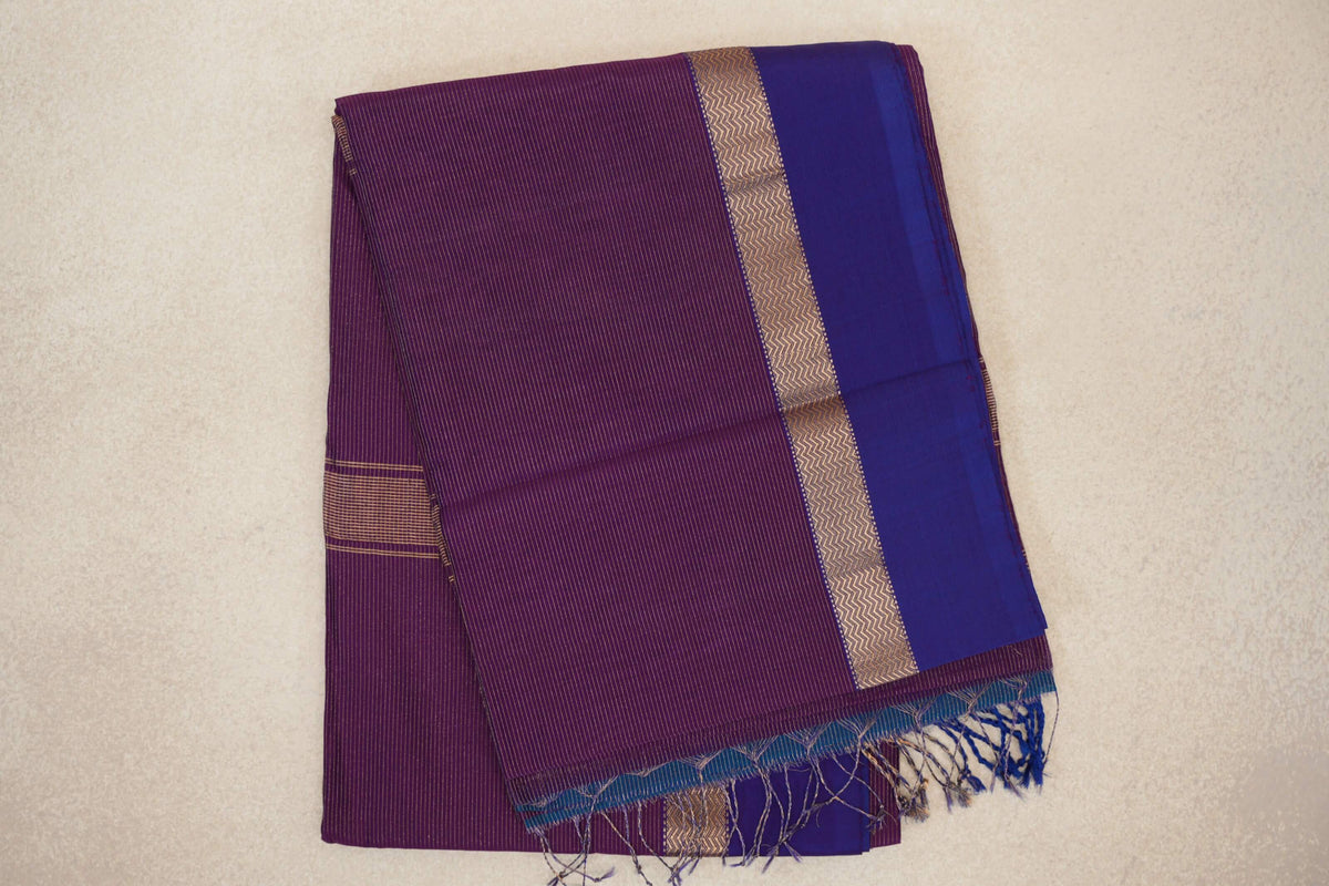 Folded Maheshwari silk cotton saree with fine stripes on deep purple, a violet purple border, a gold zigzag band and tassels.
