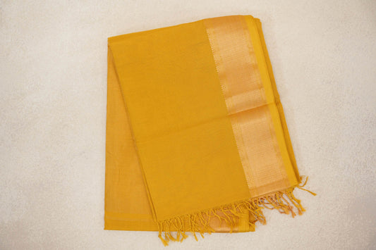 Folded mustard yellow Maheshwari silk cotton saree with a fine checked texture, a lustrous woven border and tassels at the end.