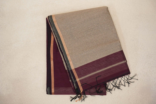Folded Maheshwari silk cotton saree showing a finely striped sandal beige pallu with a wine maroon band and dark tassels over the wine maroon body.