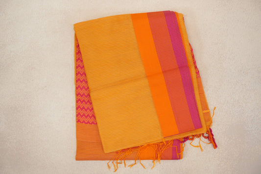 Folded mango yellow Maheshwari silk cotton saree with fine stripes, an orange and rani pink border, tassels and a pink zigzag panel peeking beneath.
