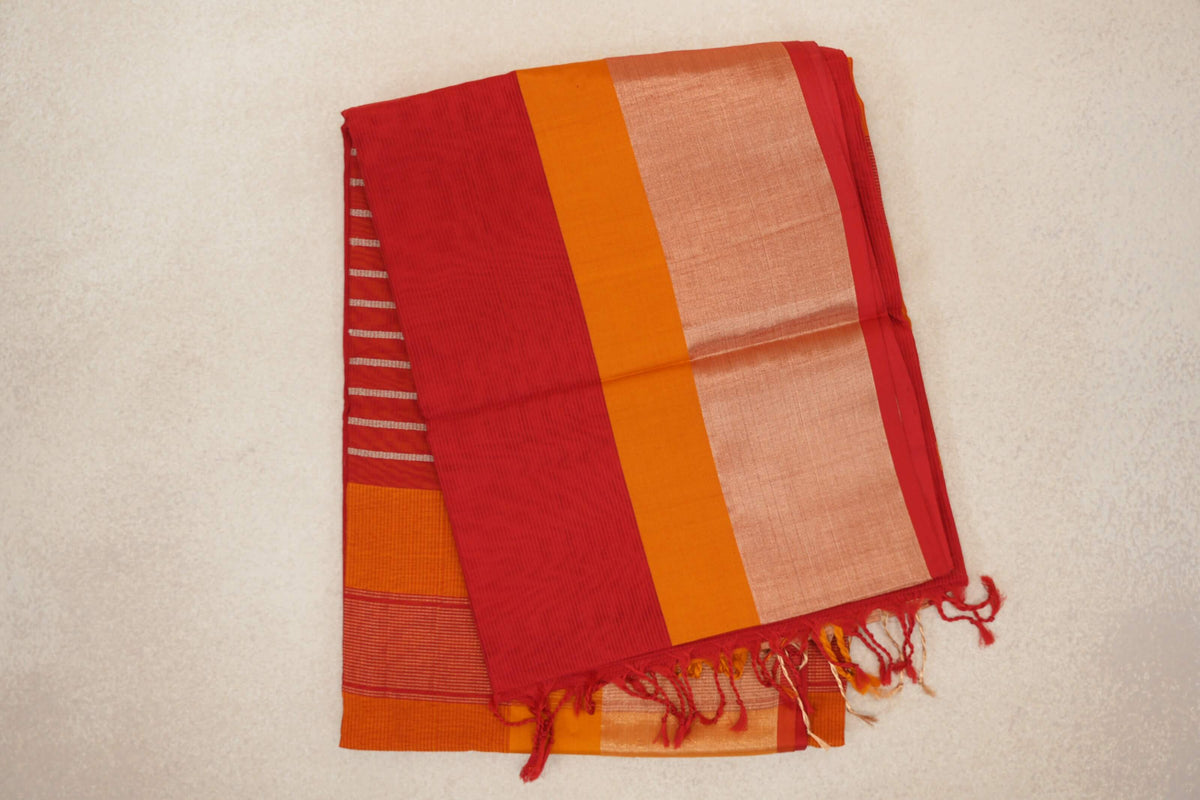 Folded Maheshwari silk cotton saree showing a tomato red pallu with fine stripes, a deep orange band, a pale shimmering panel and tassels.