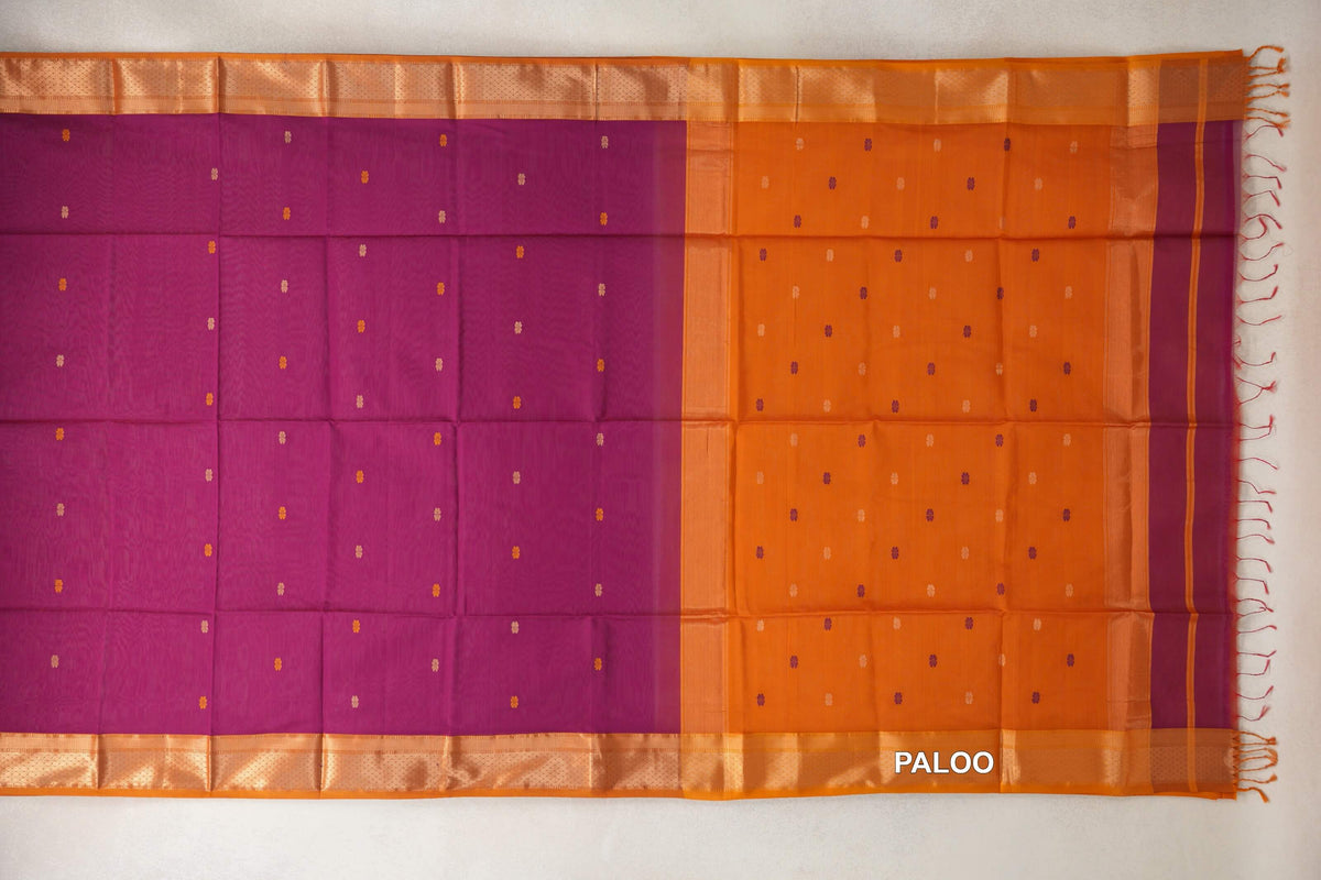Maheshwari silk cotton saree laid flat, with a dark magenta body, deep orange pallu, scattered small motifs, patterned borders and tassels.
