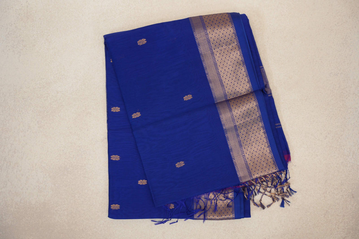 Folded bright royal blue Maheshwari silk cotton saree with small gold-toned motifs, a geometric border and tassels at one end.