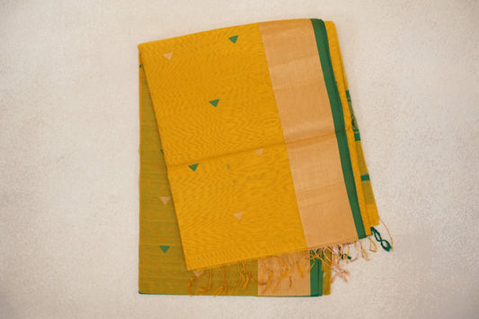 Folded turmeric yellow Maheshwari silk cotton saree with small green and pale triangles, a wide pale yellow border, bottle green edge and tassels.