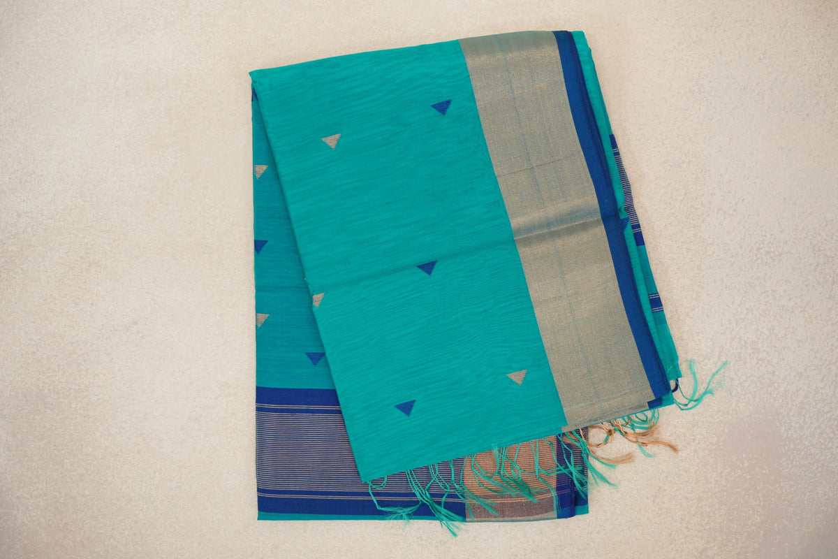 Folded bright turquoise green Maheshwari silk cotton saree with small triangular motifs, a pale metallic border, Classic Blue edging and tassels.
