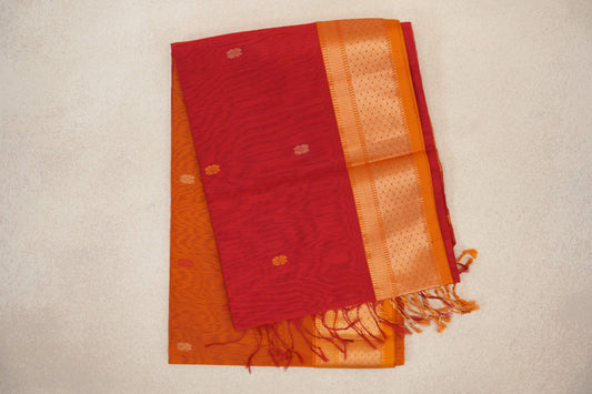 Folded Maheshwari silk cotton saree with tomato red and mustard orange layers, small woven motifs, a patterned orange border and tassels.