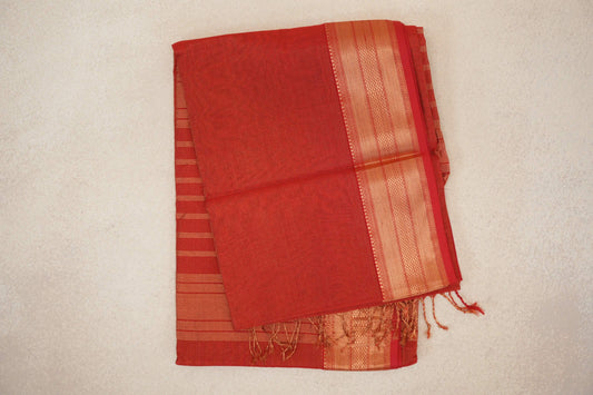 Folded tomato red Maheshwari silk cotton saree with fine gold stripes, a broad patterned border and tassels along one edge.