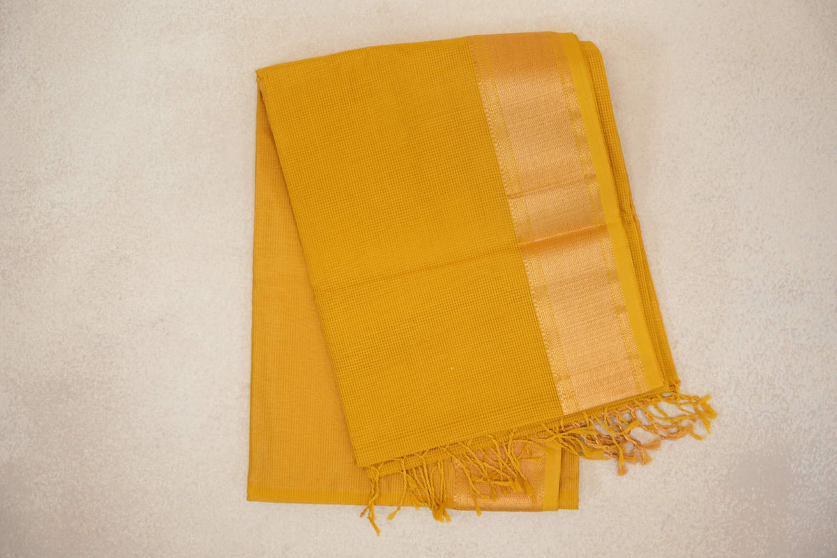 Folded turmeric yellow Maheshwari silk cotton saree with a fine checked weave, a lustrous woven border and tasselled end.