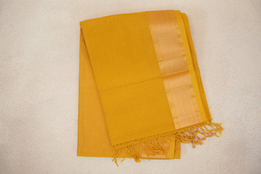 Folded turmeric yellow Maheshwari silk cotton saree with a fine checked weave, a lustrous woven border and tasselled end.