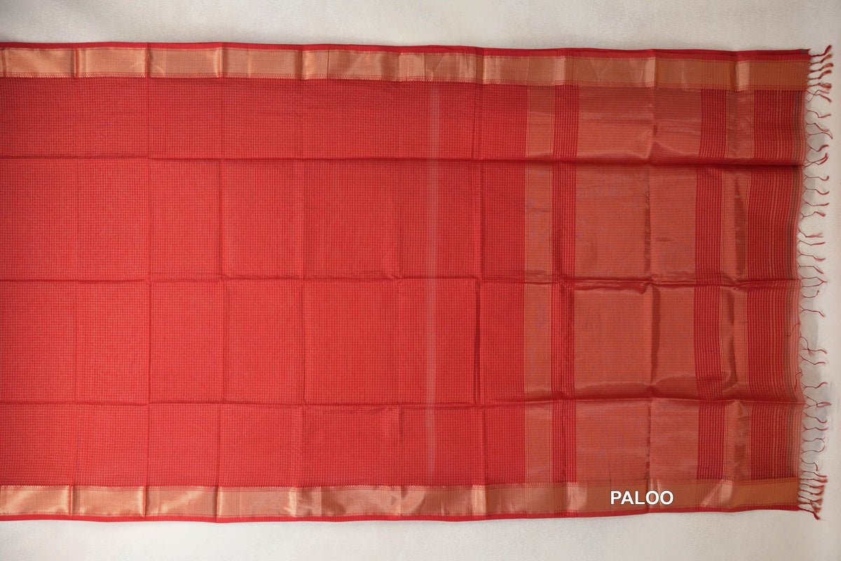 Tomato red Maheshwari silk cotton saree laid flat, with a fine checked body, gold zari borders and a striped pallu with red tassels.