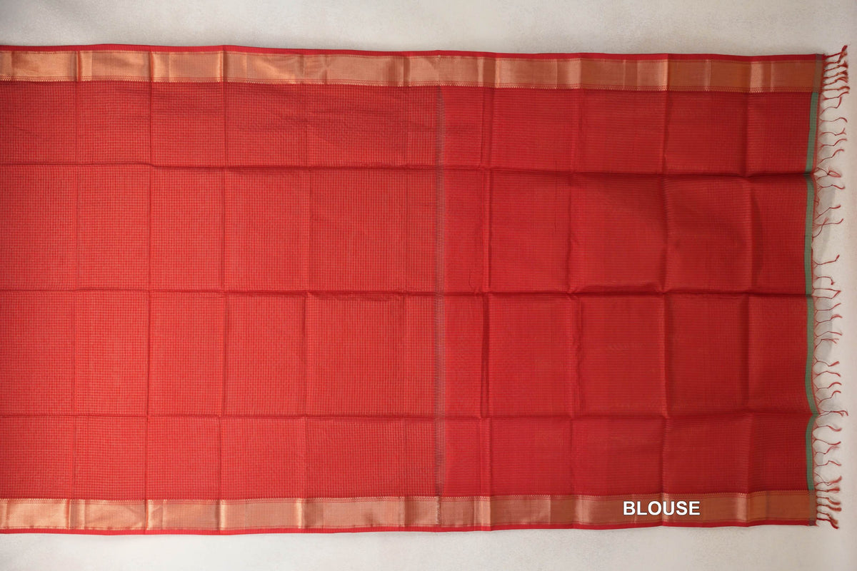 Tomato red Maheshwari silk cotton saree spread flat, showing a finely checked body, gold zari borders and a matching blouse section with tassels.