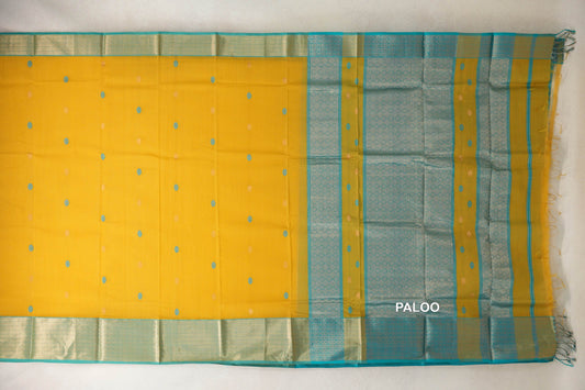 Maheshwari silk-cotton saree laid flat, with a mango yellow body, small scattered motifs, turquoise blue patterned borders and a fringed pallu.