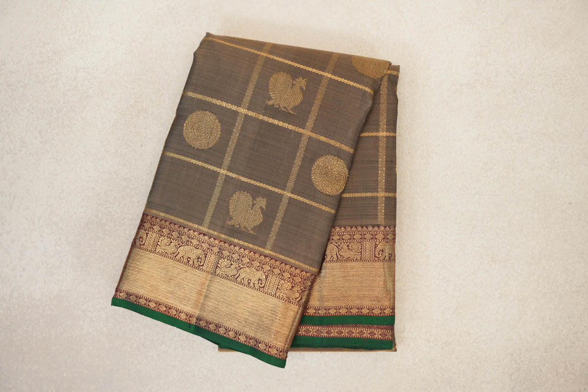 Folded olive green Kanjivaram silk saree with gold checks, bird and circular motifs, and a deep maroon and gold border edged in bottle green.