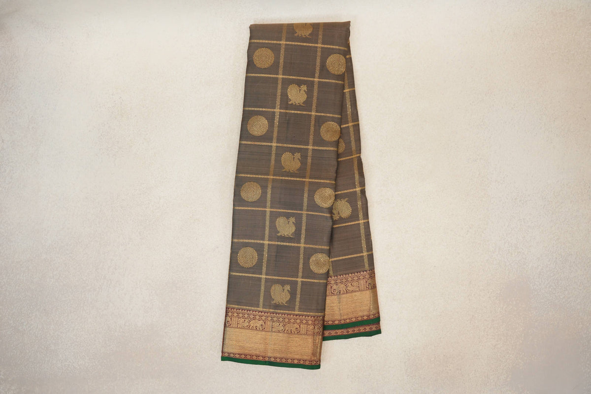Folded olive green Kanjivaram silk saree with a gold grid, circular and bird motifs, and deep maroon borders edged in bottle green.