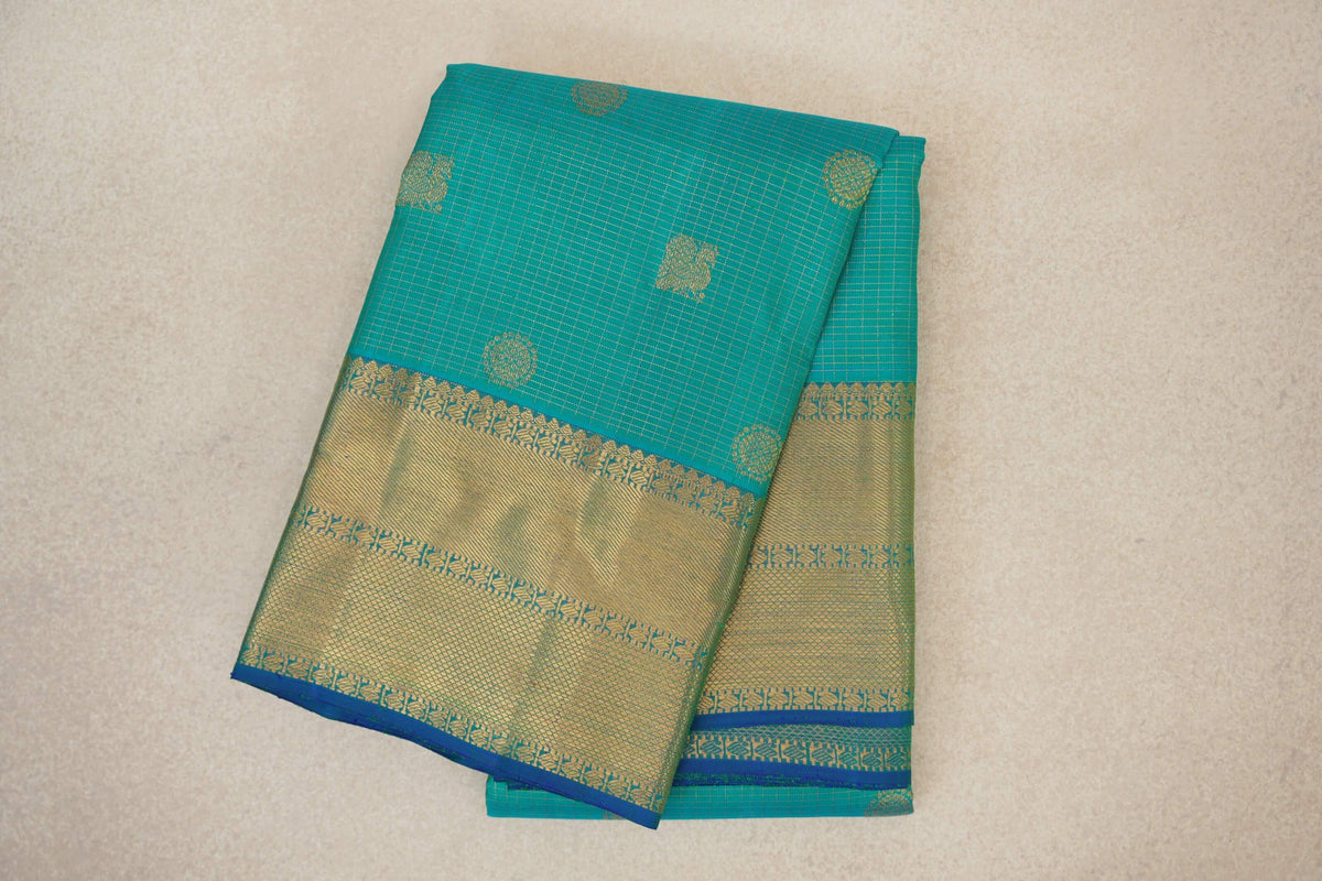 Folded aqua green Kanjivaram silk saree with fine gold checks, scattered circular motifs and a broad gold-patterned border edged in blue.