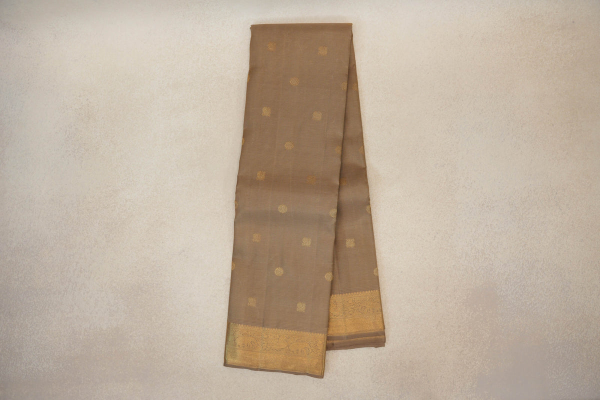 Folded greenish beige Kanjivaram silk saree with spaced gold circular motifs and a wide, intricately patterned gold border.
