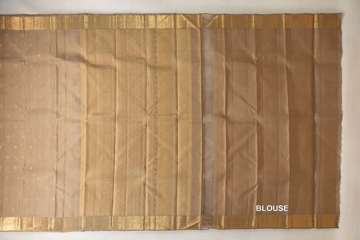 Greenish beige Kanjivaram silk saree laid out with a dotted body, patterned pallu and gold-toned borders, beside matching blouse fabric.
