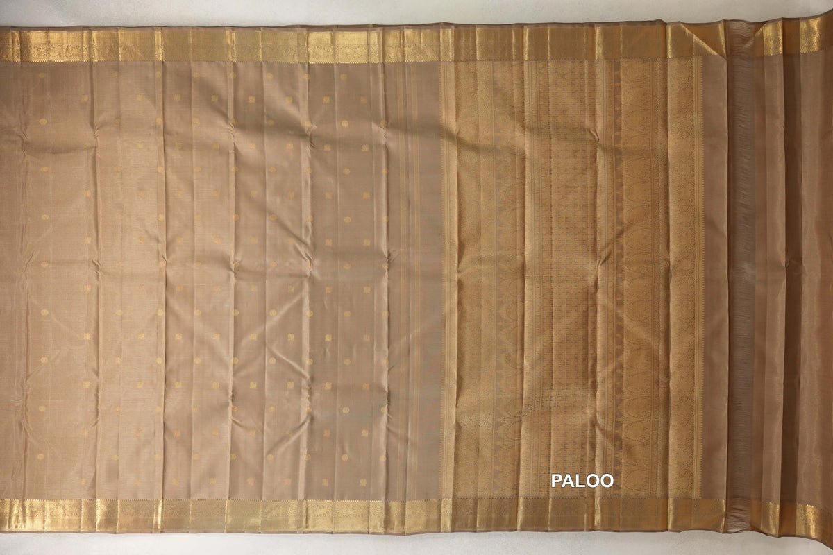 Greenish beige Kanjivaram silk saree spread flat, with small gold dots across the body, woven gold borders and an ornate pallu at right.