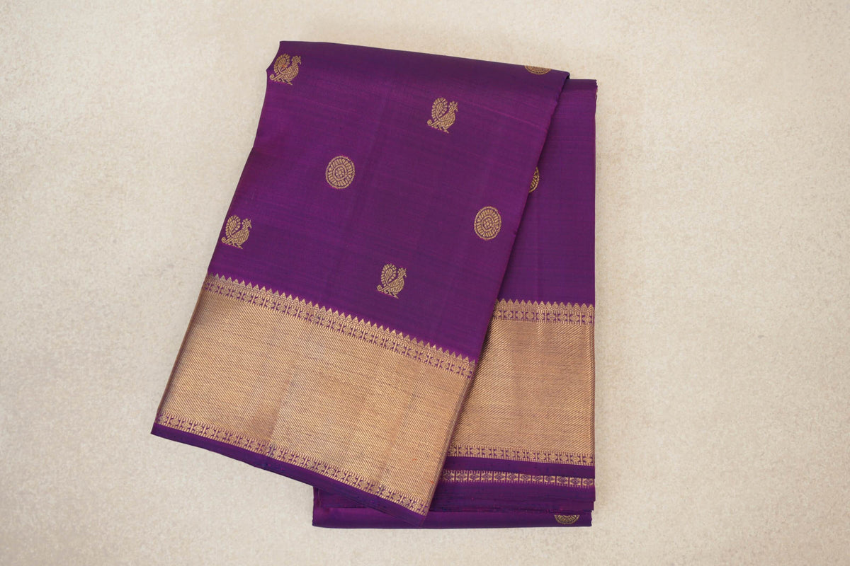 Folded purple Kanjivaram silk saree with gold bird and circular motifs and a broad gold zari border edged in purple.