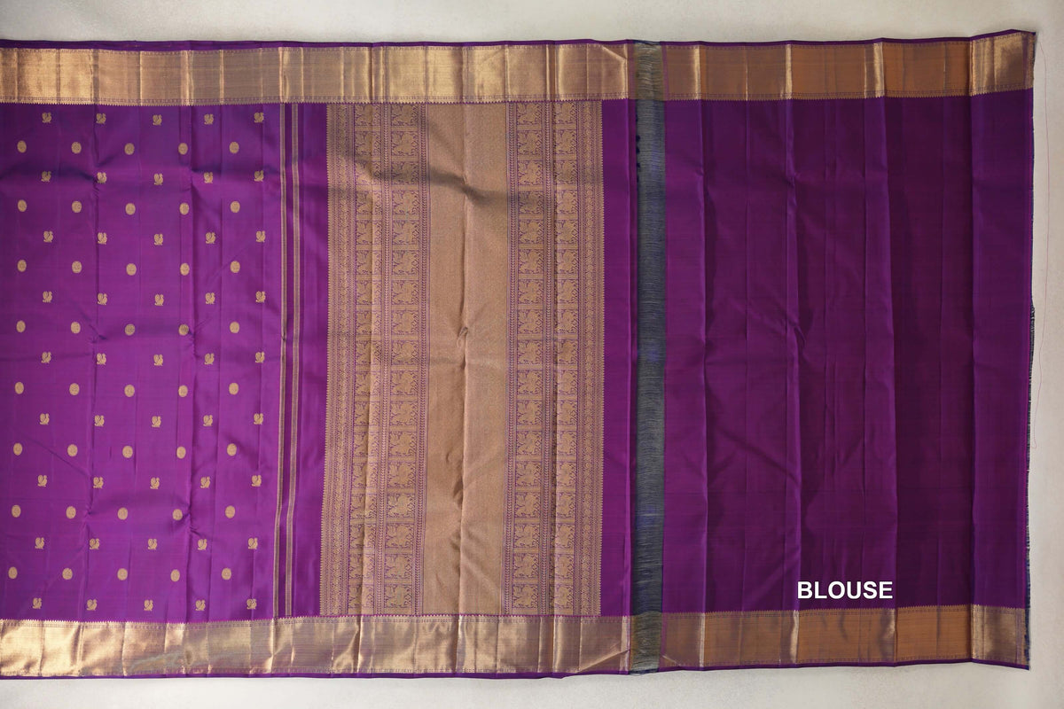 Purple Kanjivaram silk saree laid open, with small gold motifs on the body, an ornate gold pallu, broad gold borders and a plain purple blouse piece.