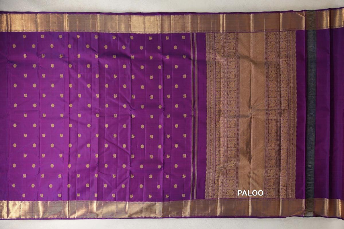Purple Kanjivaram silk saree laid flat, with rows of small gold motifs, broad gold borders and an ornate gold-woven pallu.