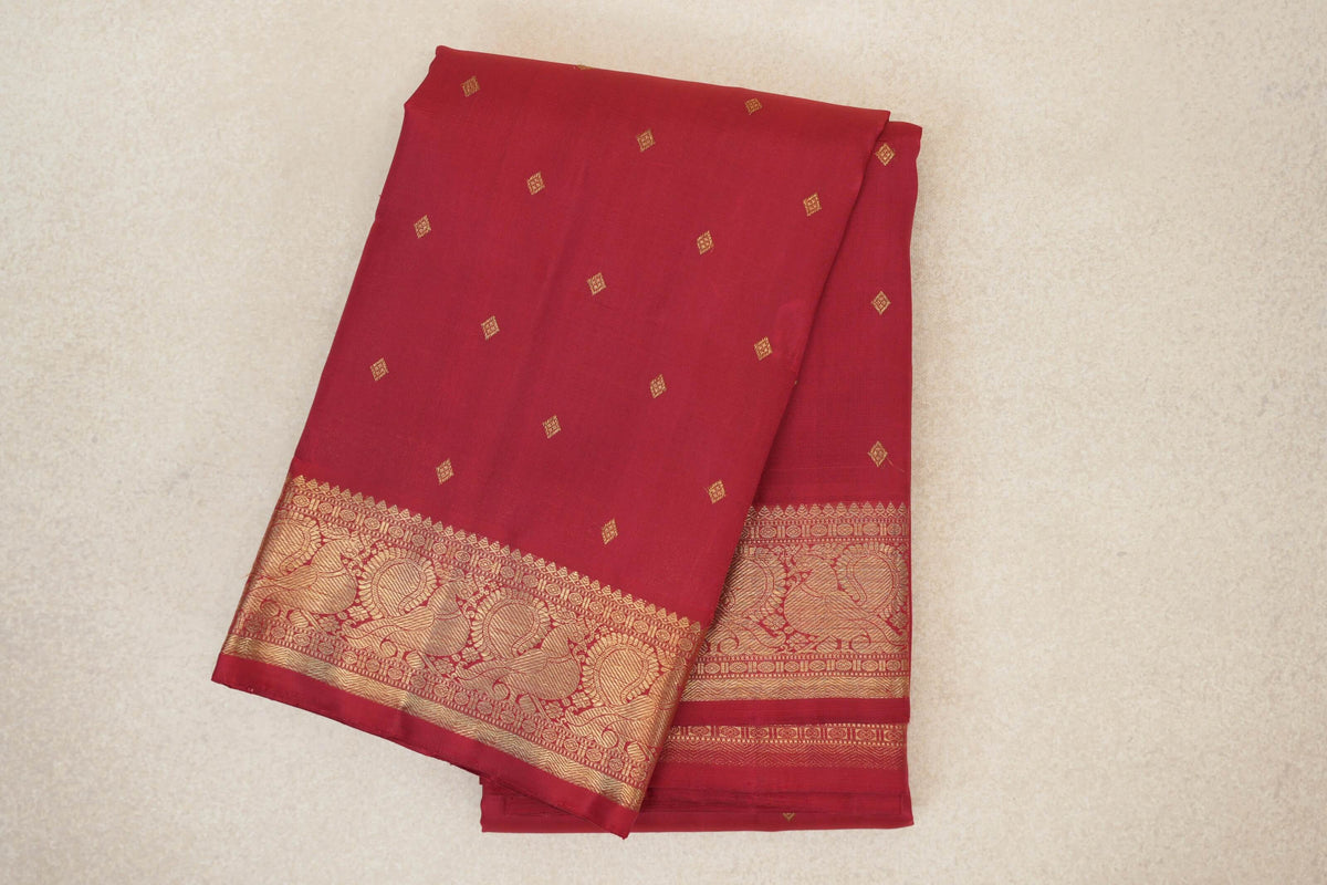 Folded crimson red heirloom Kanjivaram silk saree with scattered gold diamond motifs and an ornate gold paisley border.