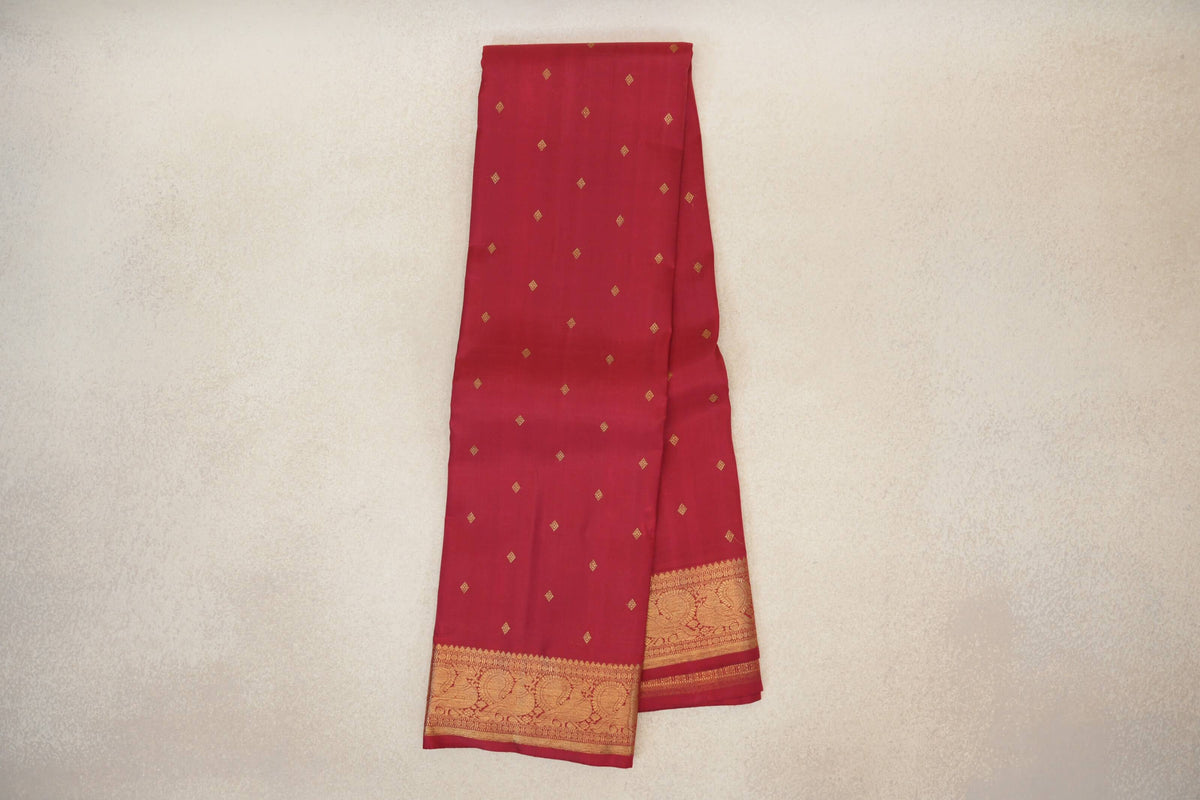 Folded crimson red Kanjivaram silk saree with small gold diamond motifs and a wide gold border featuring peacocks.