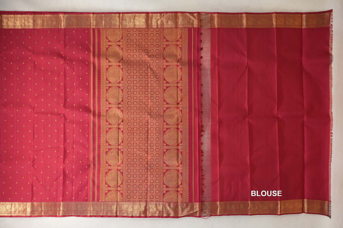 Crimson red heirloom Kanjivaram silk saree laid out with a dotted body, gold-patterned pallu and borders, and a matching blouse piece on the right.