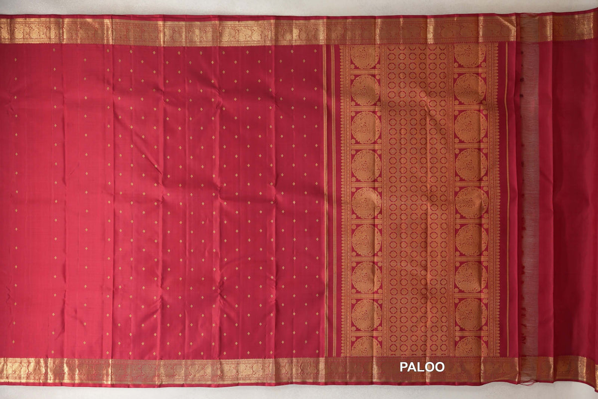Crimson red heirloom Kanjivaram silk saree laid flat, with small gold dots, ornate borders and a pallu patterned with medallions and circles.