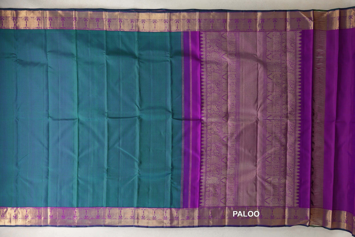 Peacock green Kanjivaram silk saree laid flat, showing purple borders with gold-toned patterns and a richly woven purple pallu.