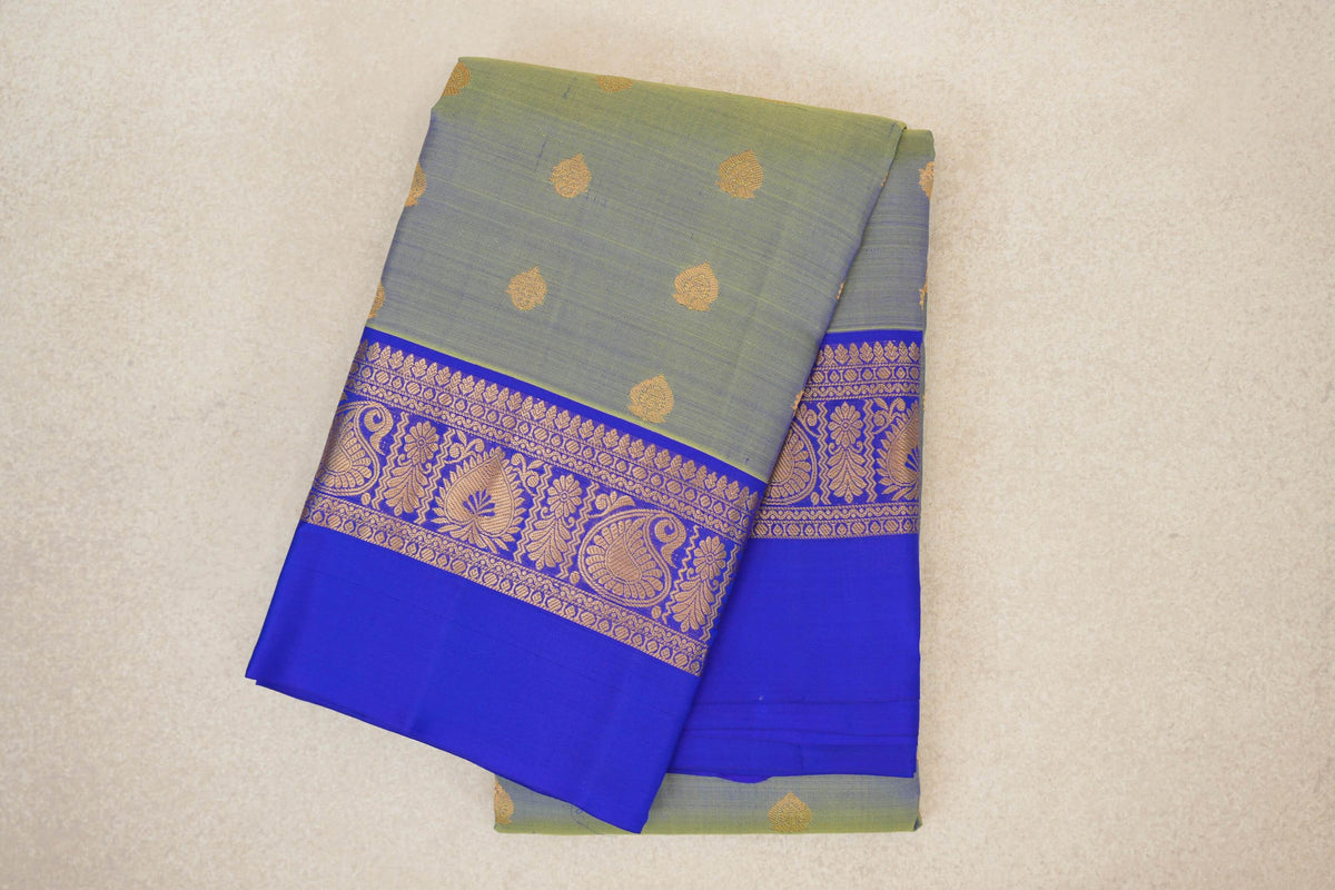 Folded light weight Kanchipuram silk saree with a yellowish green body, scattered gold-toned motifs and a royal blue border with paisley and floral designs.