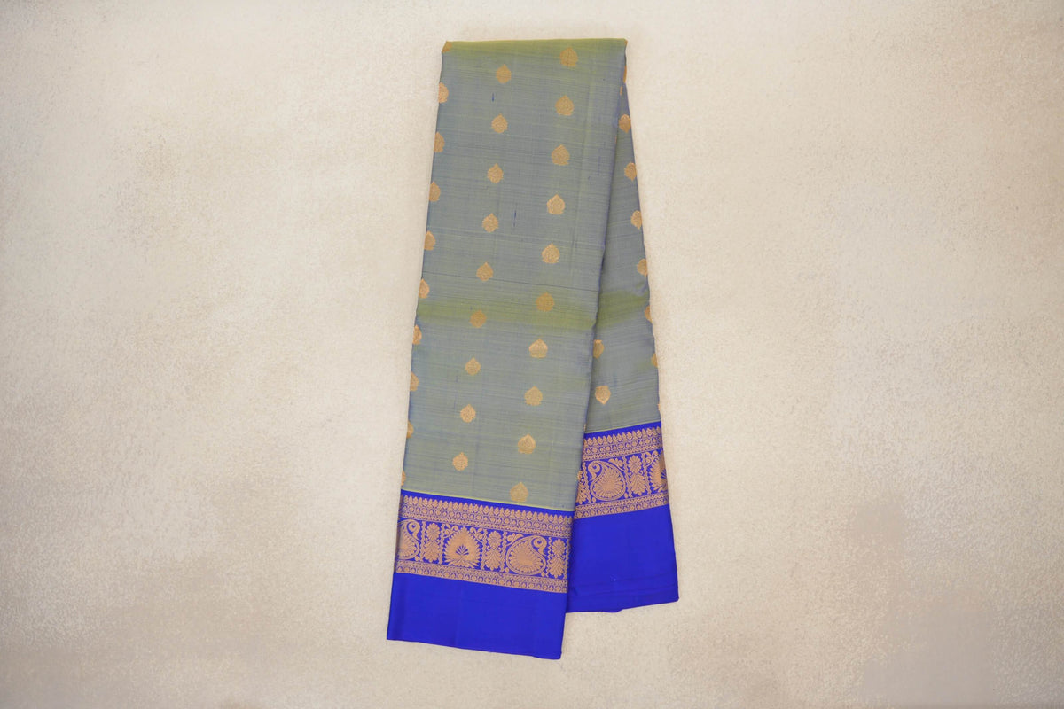 Folded yellowish green Kanchipuram silk saree with small gold motifs and a royal blue border patterned with gold paisley and floral designs.