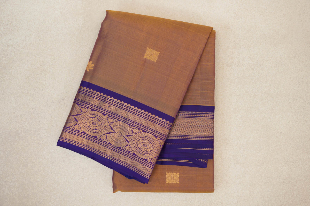 Folded light weight Kanchipuram silk saree with a magenta and yellow body, small gold-toned motifs and an ornate violet purple border.