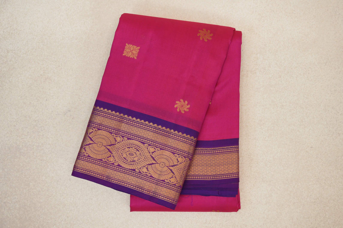 Folded rani pink lightweight Kanchipuram silk saree with scattered gold floral motifs and ornate gold-patterned magenta purple borders.