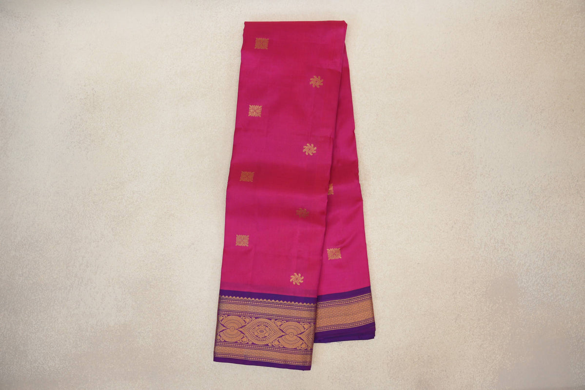 Folded rani pink light weight Kanchipuram silk saree with scattered gold motifs and a magenta purple border with gold woven patterns.