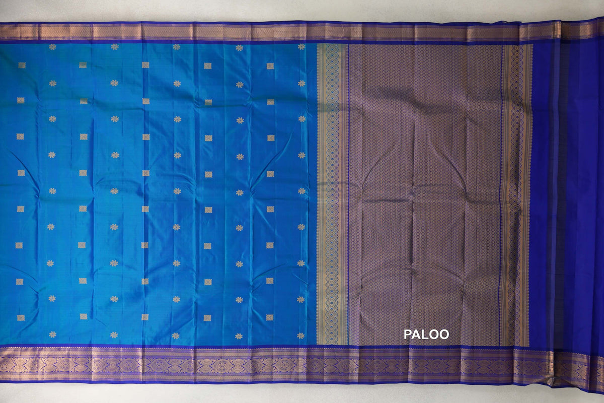 Light Weight Kanchipuram silk saree spread open, with a peacock blue body dotted with small motifs and a patterned deep royal blue pallu and borders.