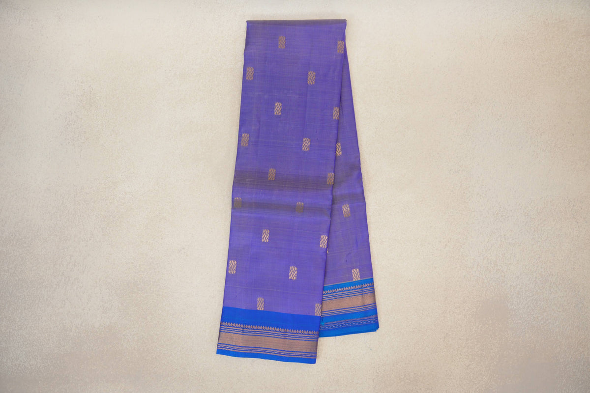 Folded lavender Kanchipuram silk saree with spaced gold geometric motifs and a royal blue border with fine gold patterned stripes.