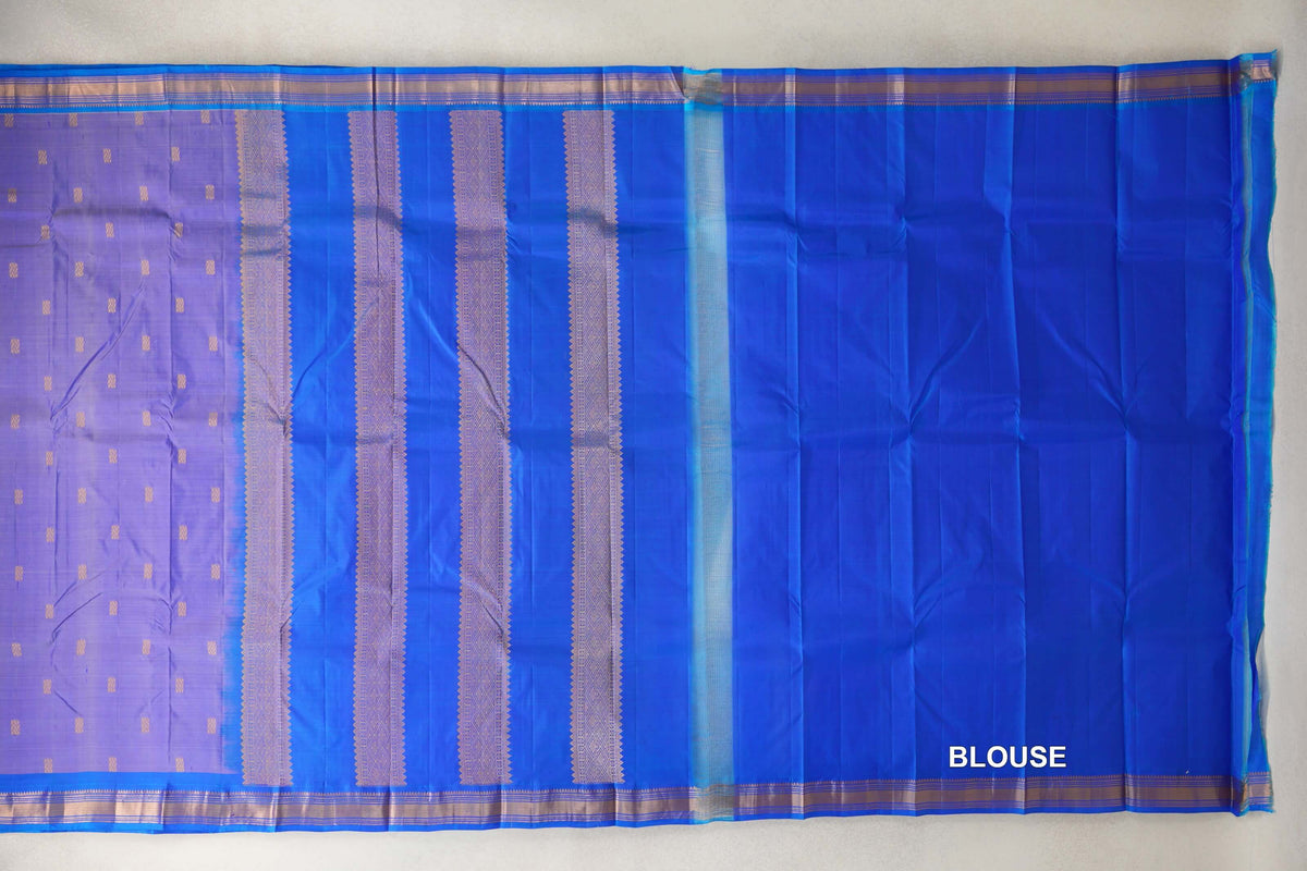 Laid-out lavender Kanchipuram silk saree with small motifs, a royal blue pallu with patterned vertical bands, and a plain blue blouse piece.